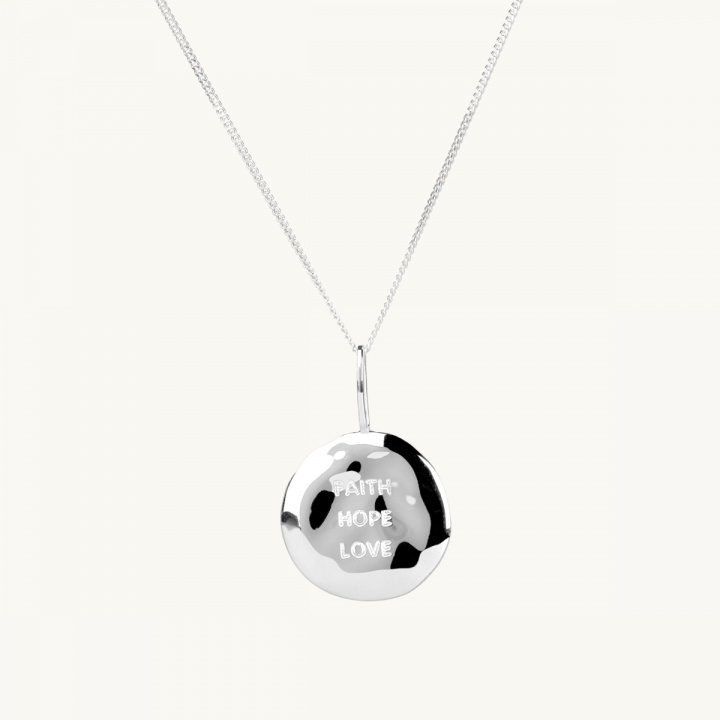 Ett mynt i silver med bucklig yta och texten faith, hope, love